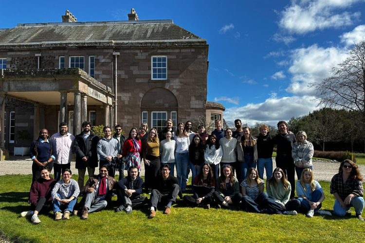 The picture shows students gathered outside The Burn building, with beautiful sunshine and blue skies.